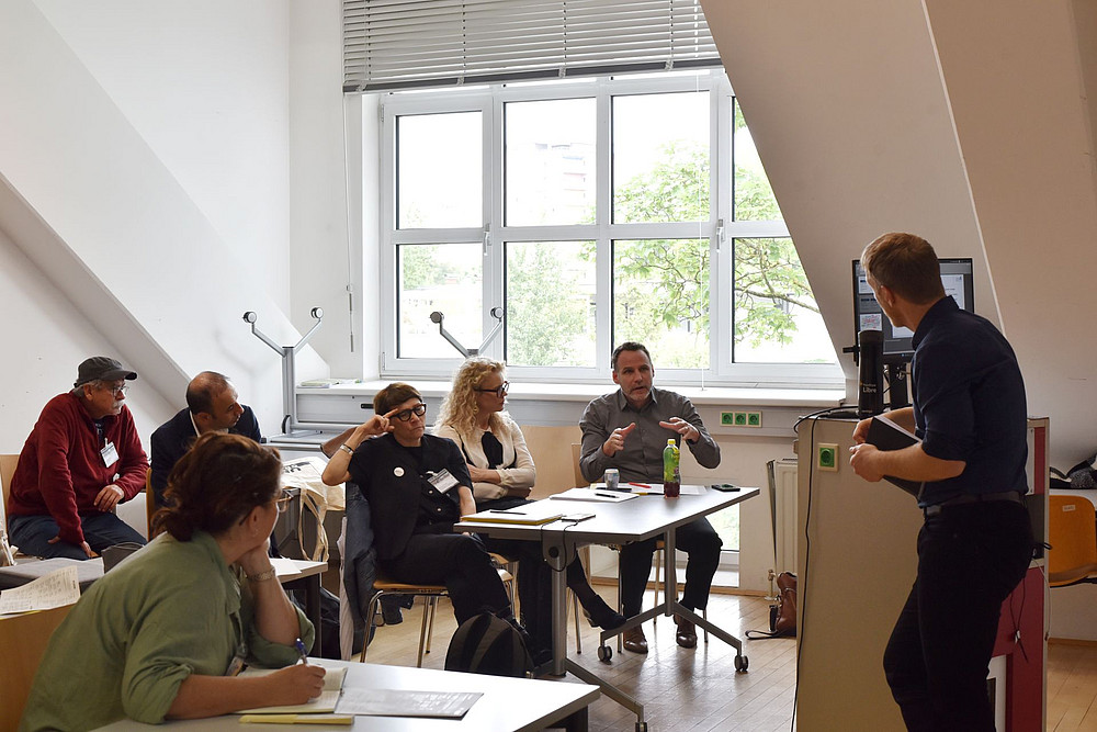 6 Leute sitzen an Tischen in einem Seminarraum und sprechen mit einem Mann, der vorne am Rednerpult steht ©Uni Graz/Anđela Karać
