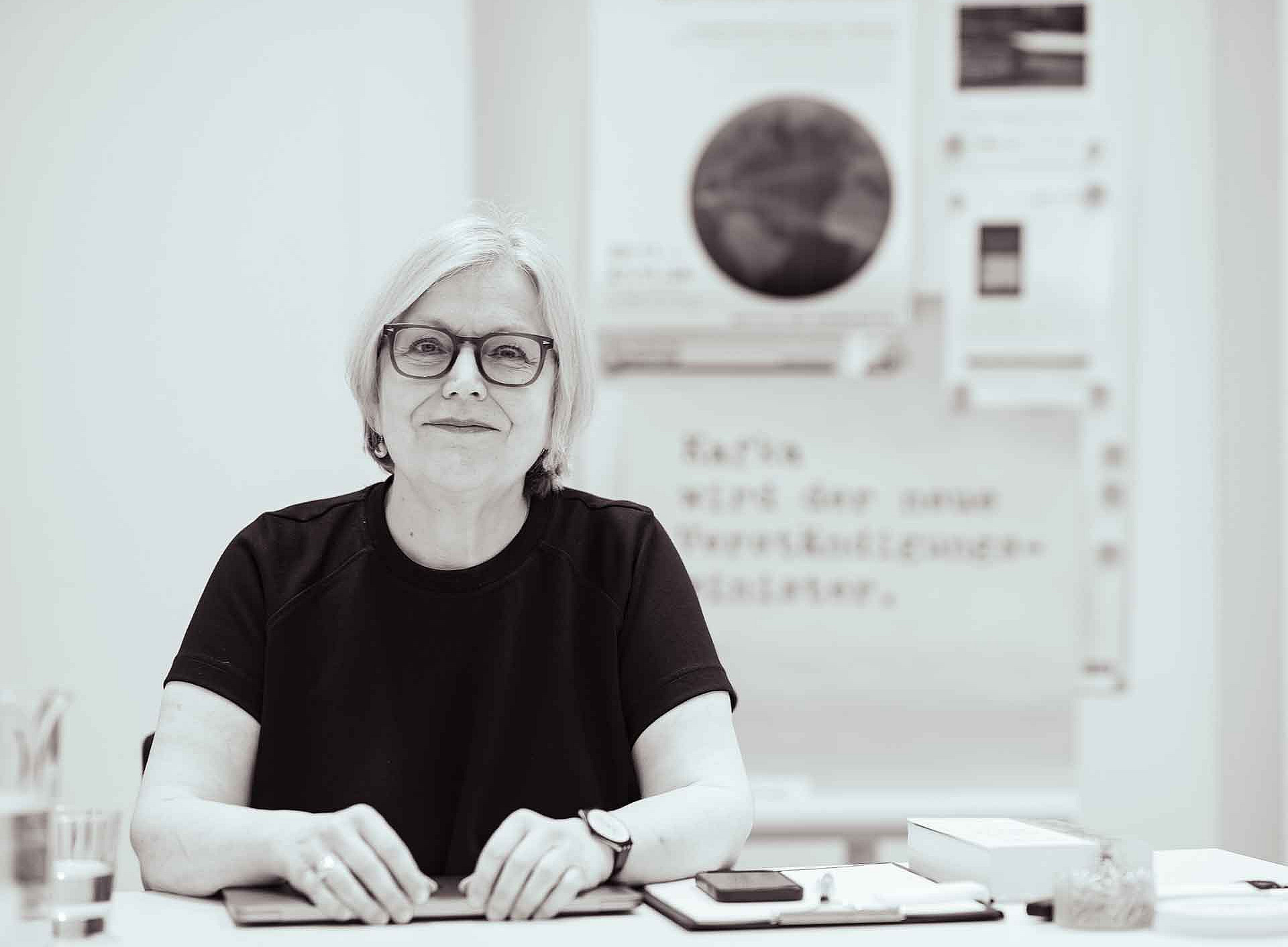 A woman wearing glasses is sitting at a table and smiling at the camera ©Uni Graz/Tzivanopoulos