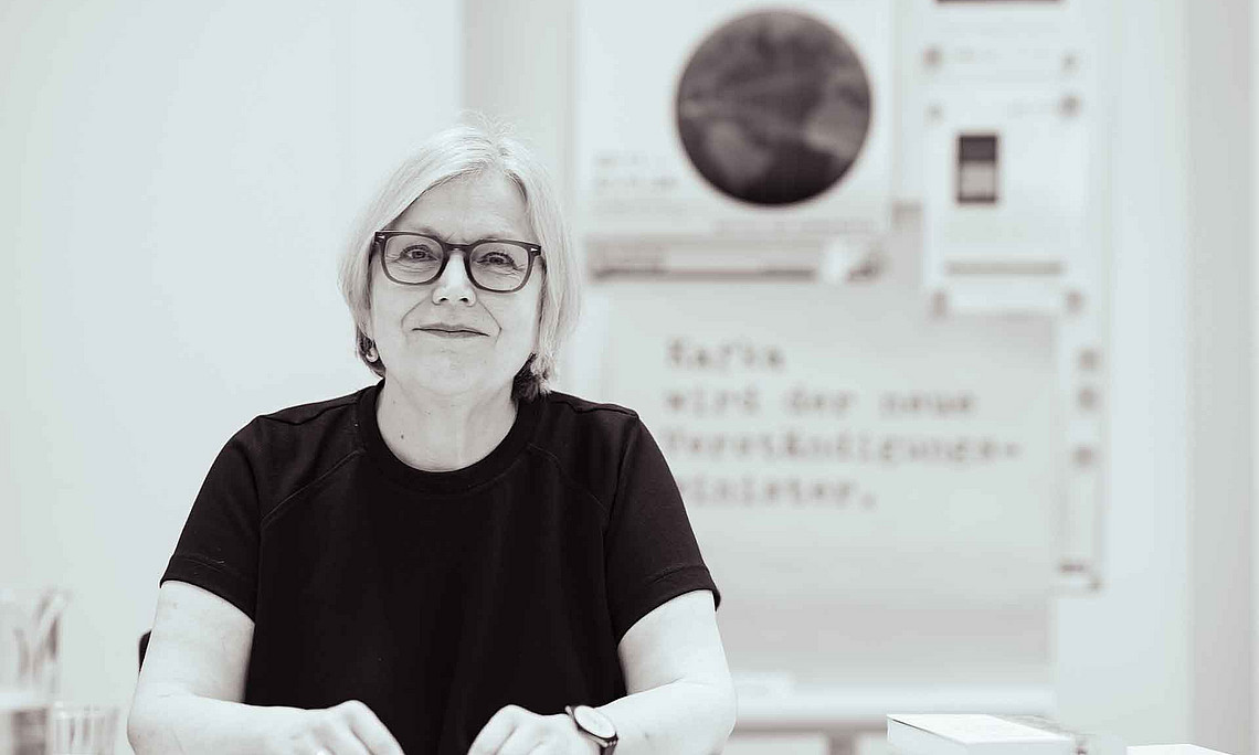 Eine Frau mit Brille sitzt am Tisch und lächelt in die Kamera