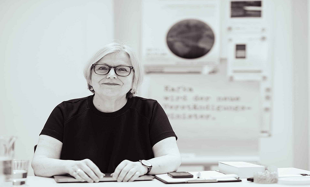 Eine Frau mit Brille sitzt am Tisch und lächelt in die Kamera