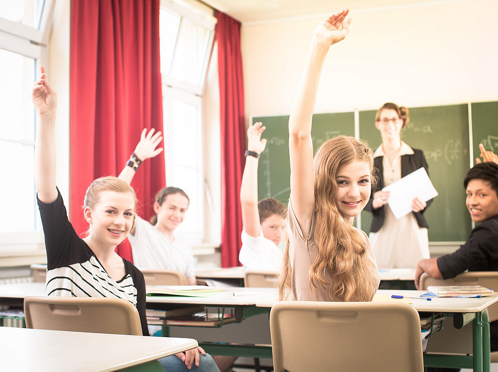 Schülerinnen heben in einem Klassenraum die Hand und symbolisieren die abgeschlossenen Projekte der Kooperationspartner:innen ©Kzenon - stock.adobe.com