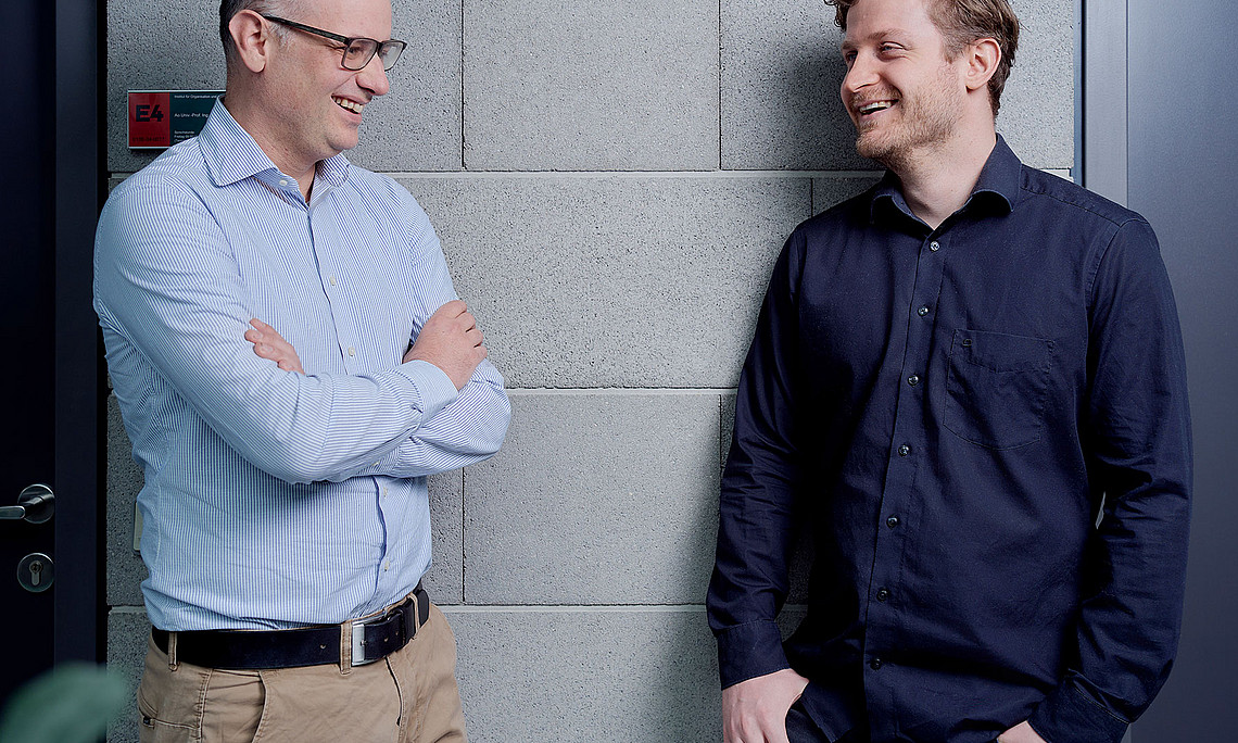 Jürgen Fleiß and Armin Haberl laughing together in front of office doors at the RESOWI Center at the University of Graz
