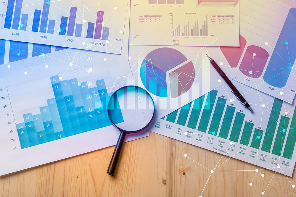 On a wooden surface are several pages of paper on which statistical diagrams are displayed. There is also a magnifying glass on the paper pages. ©tonefotografia - stock.adobe.com