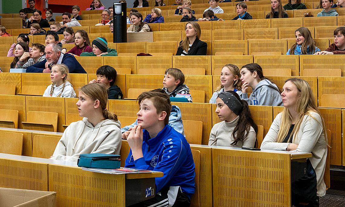 Schler sitzen in einem Hörsaal und schauen gebannt auf ein Objekt, das im bIld nicht zu sehen ist