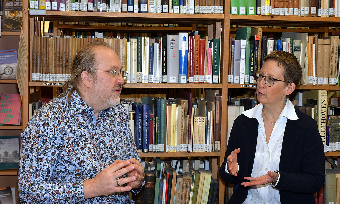 Stefan Baumgarten and Susanne Kogler in conversation, sitting at a table in front of a bookshelf