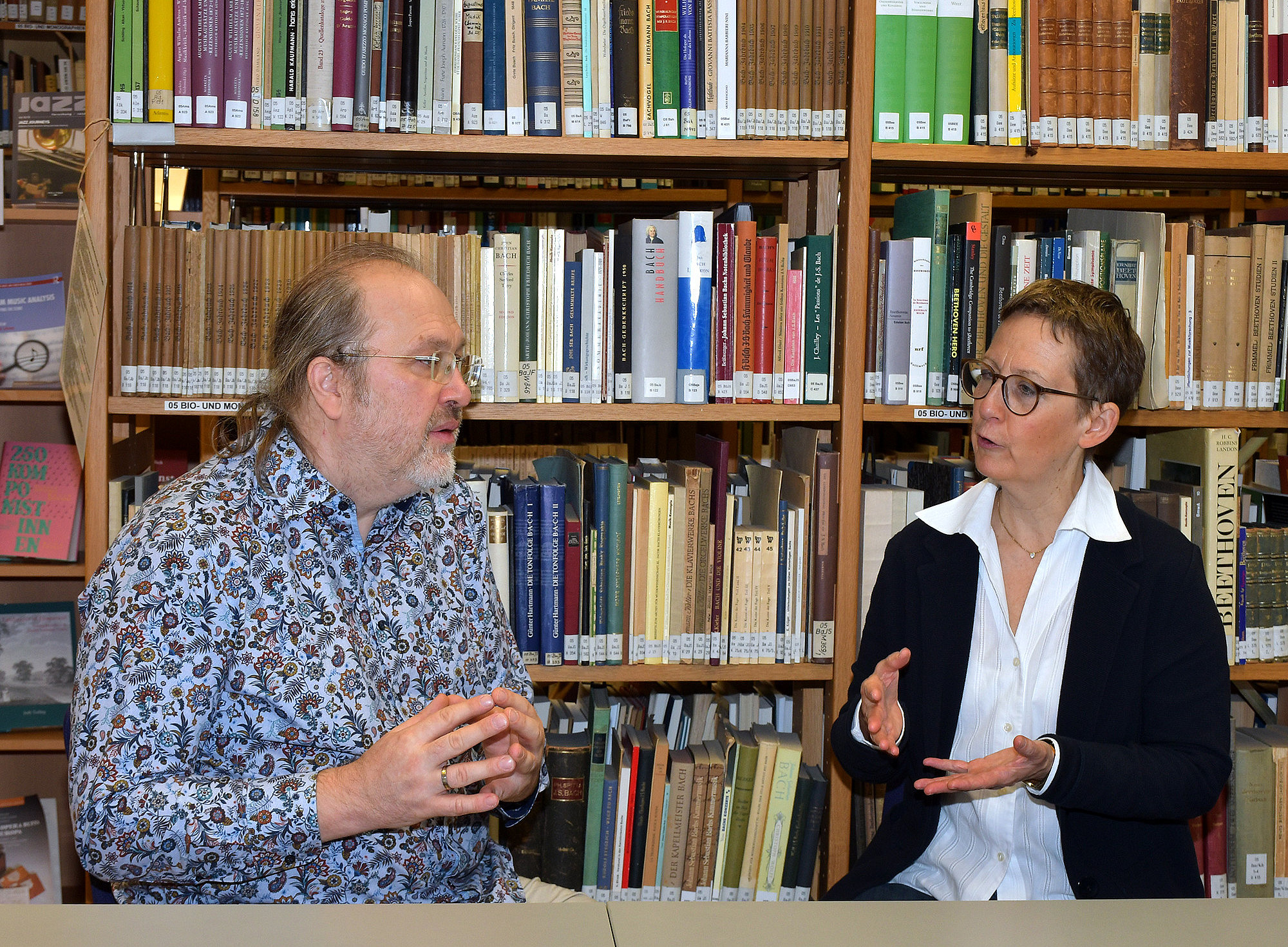 Stefan Baumgarten and Susanne Kogler in conversation, sitting at a table in front of a bookshelf ©University of Graz/Pichler