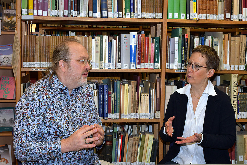 Stefan Baumgarten and Susanne Kogler in conversation, sitting at a table in front of a bookshelf