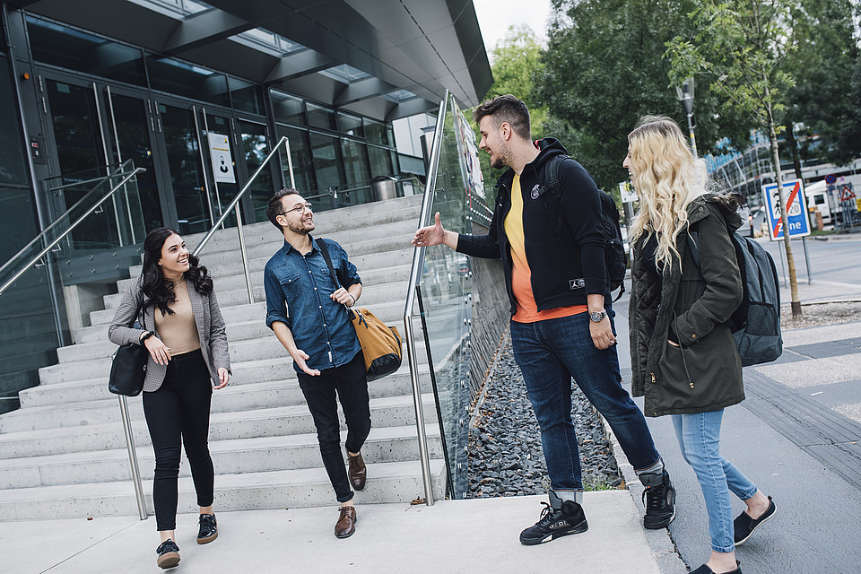 Studierende stehen vor dem Chemie-Gebäude der Uni Graz und unterhalten sich miteinander; im Hintergrund stehen Fahrräder