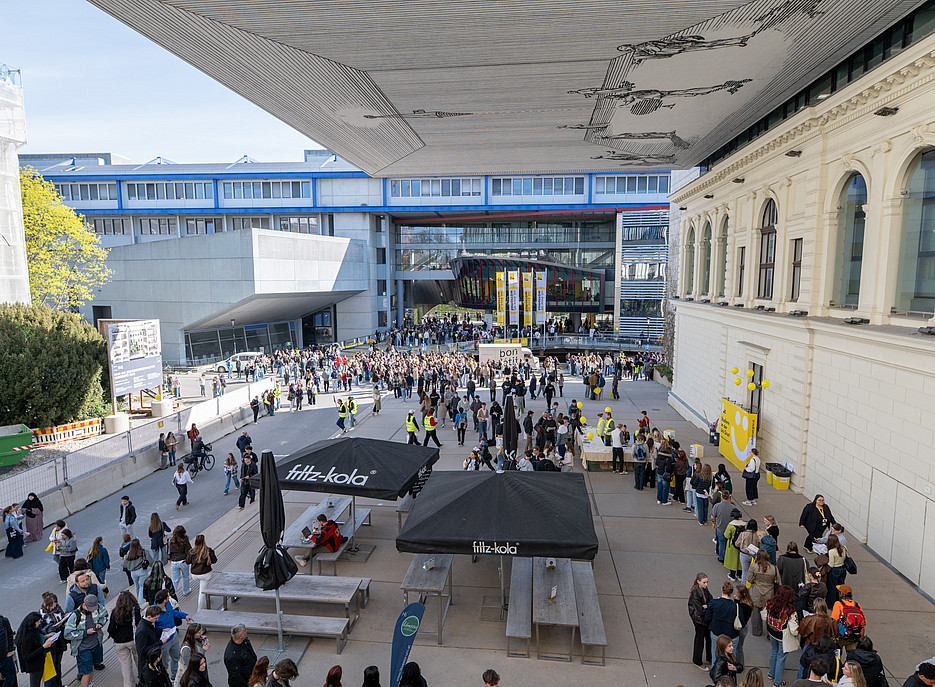 Ein großer Platz mit vielen Menschen, die teils im Schatten der Gebäude, teils in der Sonne stehen. ©Uni Graz/Angele