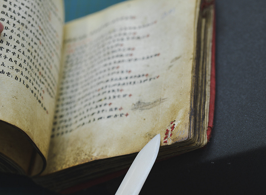 Ein Falzbein zeigt auf eine genähte Stelle in einer Handschrift ©Uni Graz/Tzivanopoulos