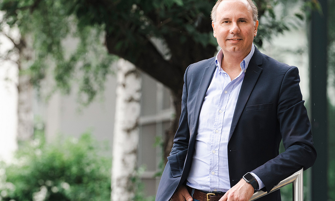 Oliver Ruppel vor einem Baum, seine linke Hand an einem Handlauf aus Edelstahl