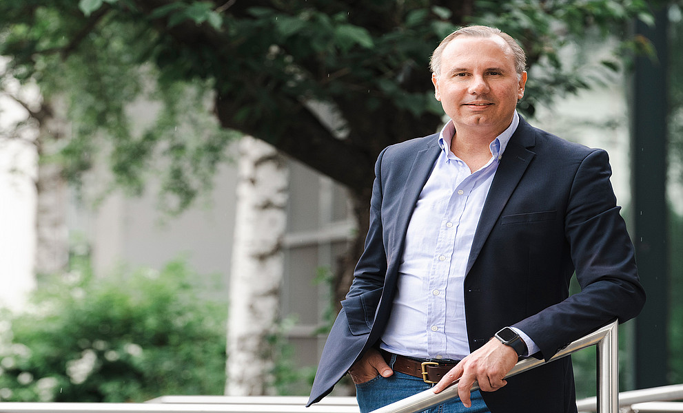 Oliver Ruppel vor einem Baum, seine linke Hand an einem Handlauf aus Edelstahl