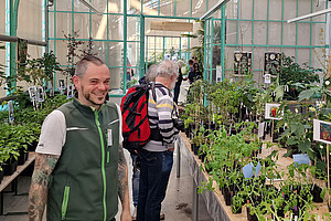Pflanzenraritätenmarkt im Botanischen Garten: zwei Personen inmitten hunderter Gemüsepflanzen im historischen Gewächshaus.