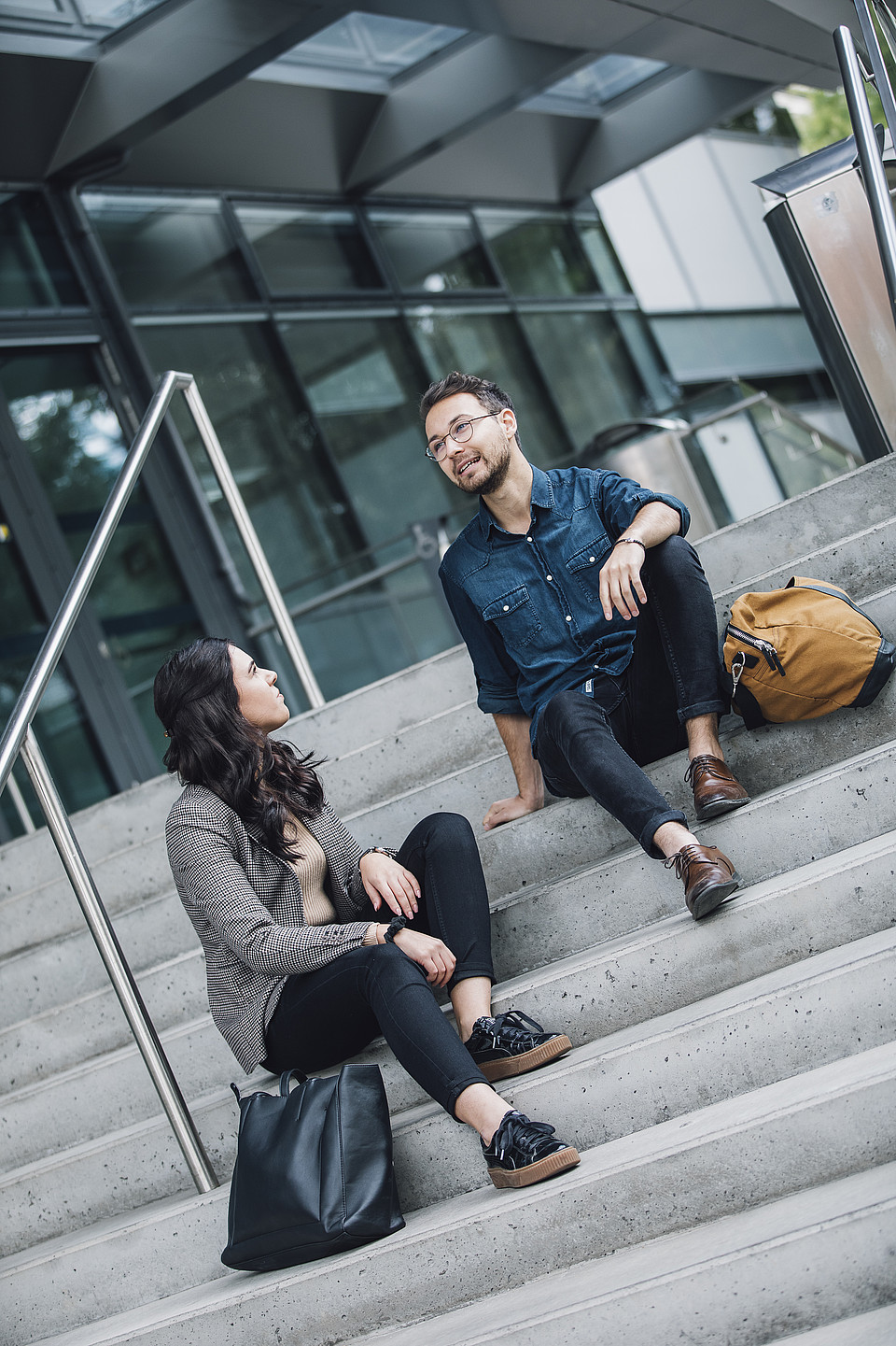Zwei Studierende sitzen draußen nebeneinander auf den Stufen eines Universitätsgebäudes und unterhalten sich ernst miteinander.