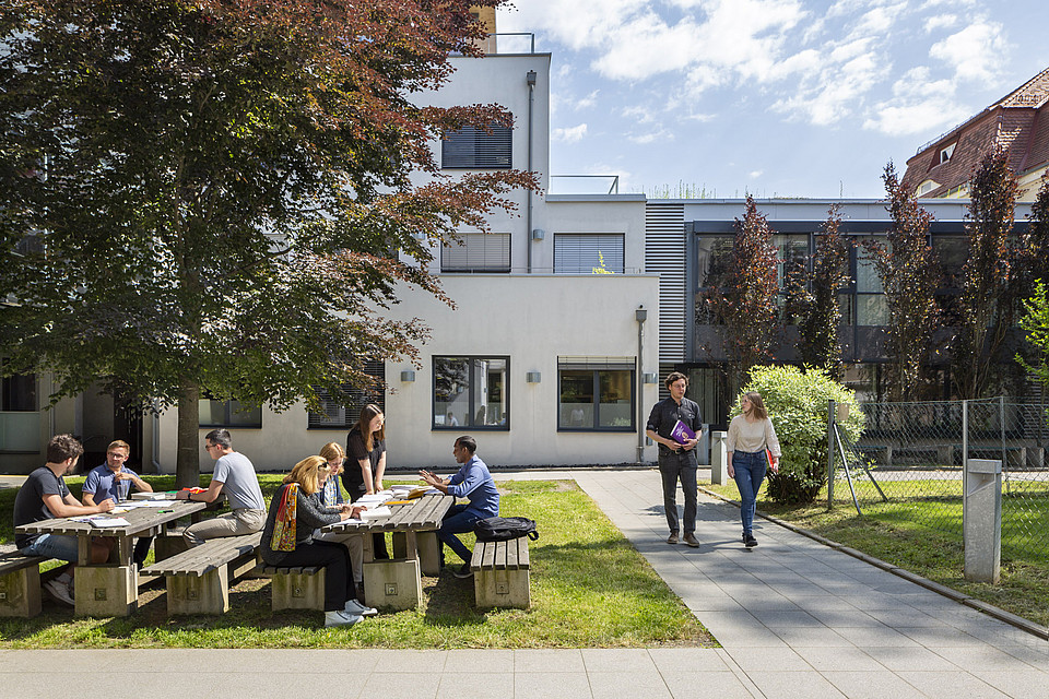 Studierende unterhalten sich im sonnigen Innenhof des Theologie-Instituts.