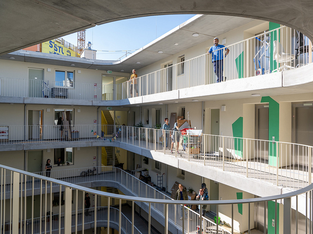 Lichtdurchfluteter Innenhof in einem Haus, das gut durchdacht ist. Jede Wohnung im Innenhof hat einen großen, gut nutzbaren Balkon. Menschen sind im Innenhof und teilweise arbeiten sie, teilweise entspannen sie. {f:if(condition: 'Luiza Puiu', then: '©Luiza Puiu')}