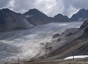 Glacier tongue surrounded by snow-free rocks and scree, lift poles in the foreground