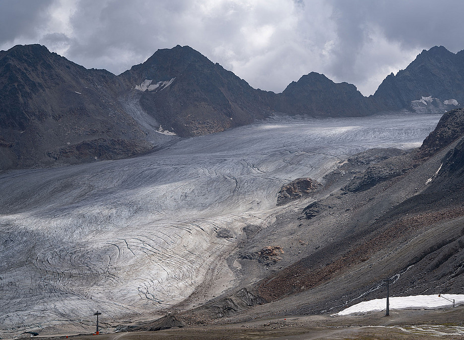 Gletscherzunge umgeben von schneefreien Felsen und Geröll, im Vordergrund Liftstützen ©Stefan Schauhuber