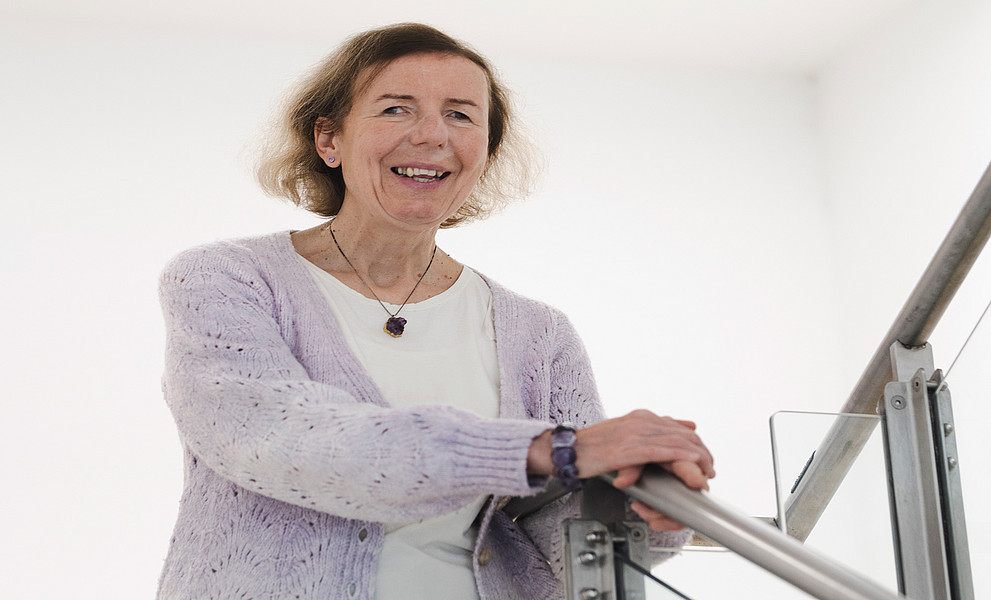 Barbara Levc vor weißem Hintergrund, die Hände auf einem Stiegengeländer aus Edelstahl