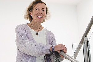 Barbara Levc in front of a white background, hands on a stainless steel staircase railing