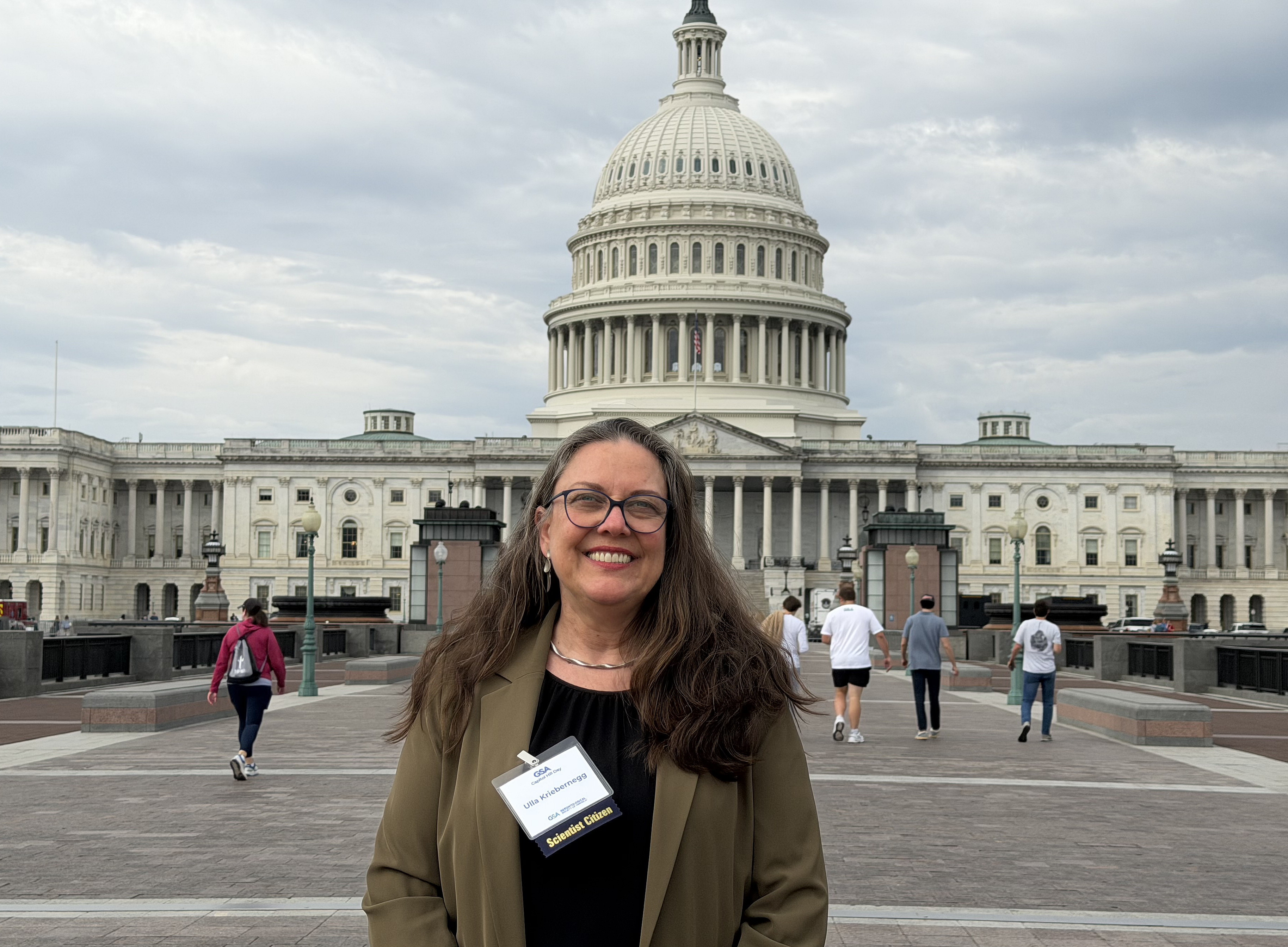 Eine Frau steht vor einem Gebäude mit einer beigen Fassade. Sie hat einen blauen Blazer an 