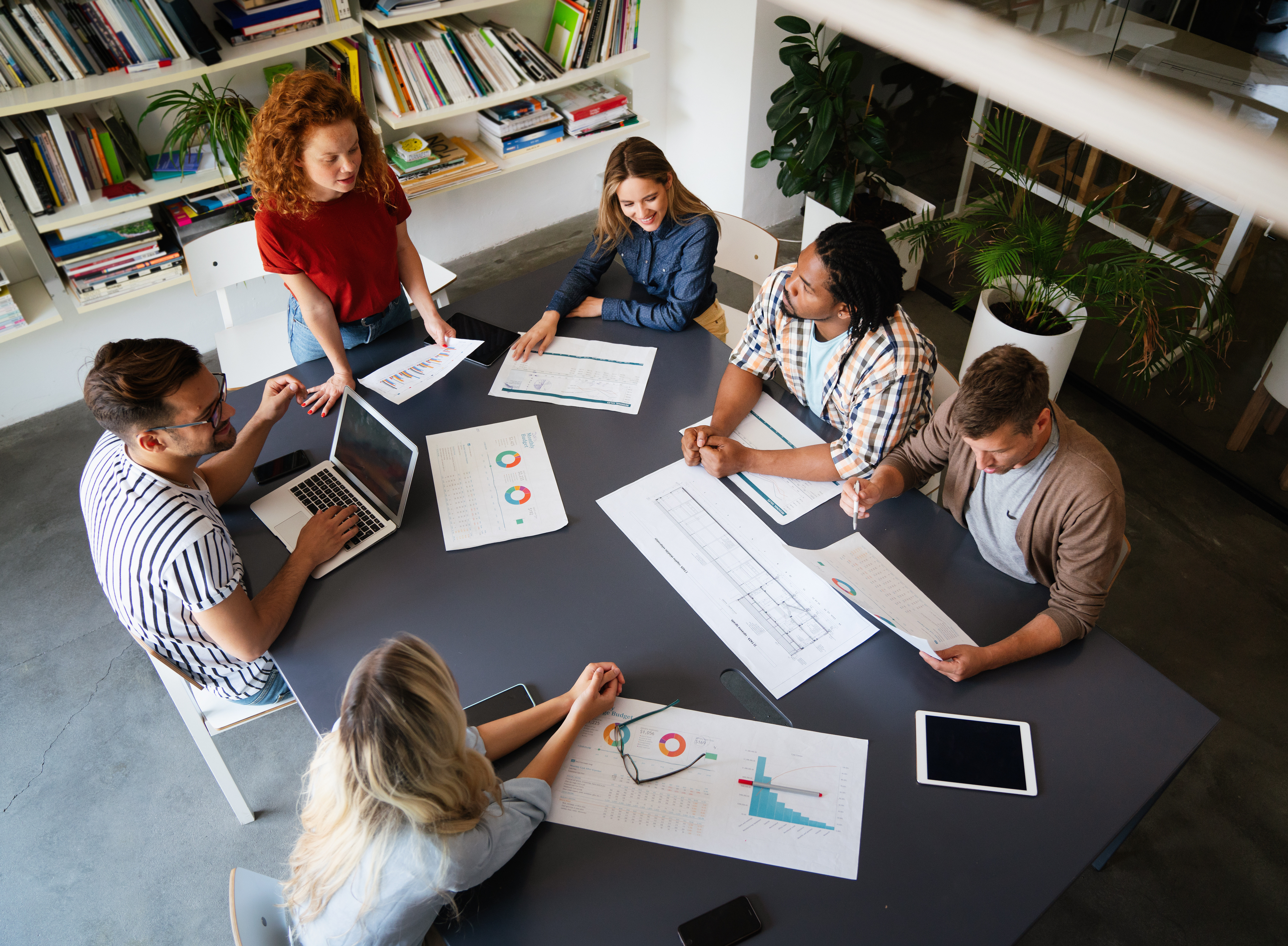 Eine Gruppe junger Menschen sitzt zusammen an einem großen Tisch und arbeitet an neuen Ideen und Konzepten. ©NDABCREATIVITY