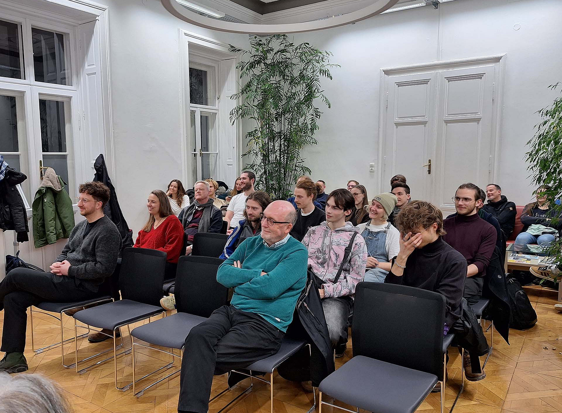Ein Raum mit hohen Decken, in dem 4 Reihen von Stühlen stehen, auf einem Großteil der Stühle sitzen Personen ©Uni Graz/Martina Mayer-Krauss