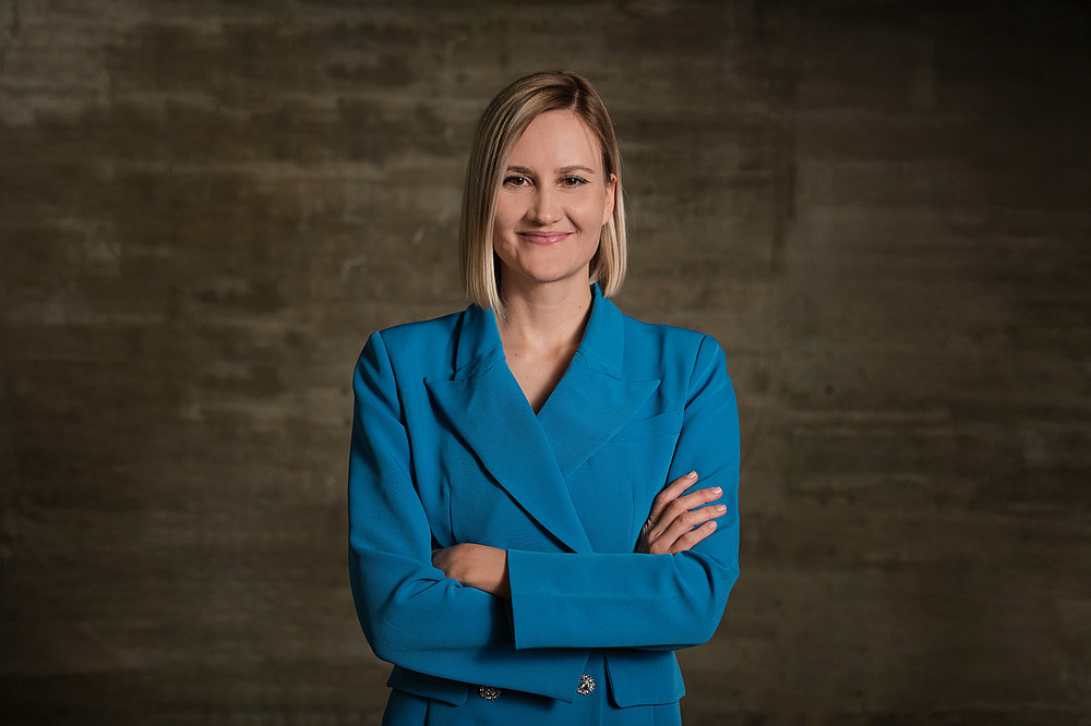 Frau Prof. Bayer in blauer Jacke vor brauner Ziegelwand 
