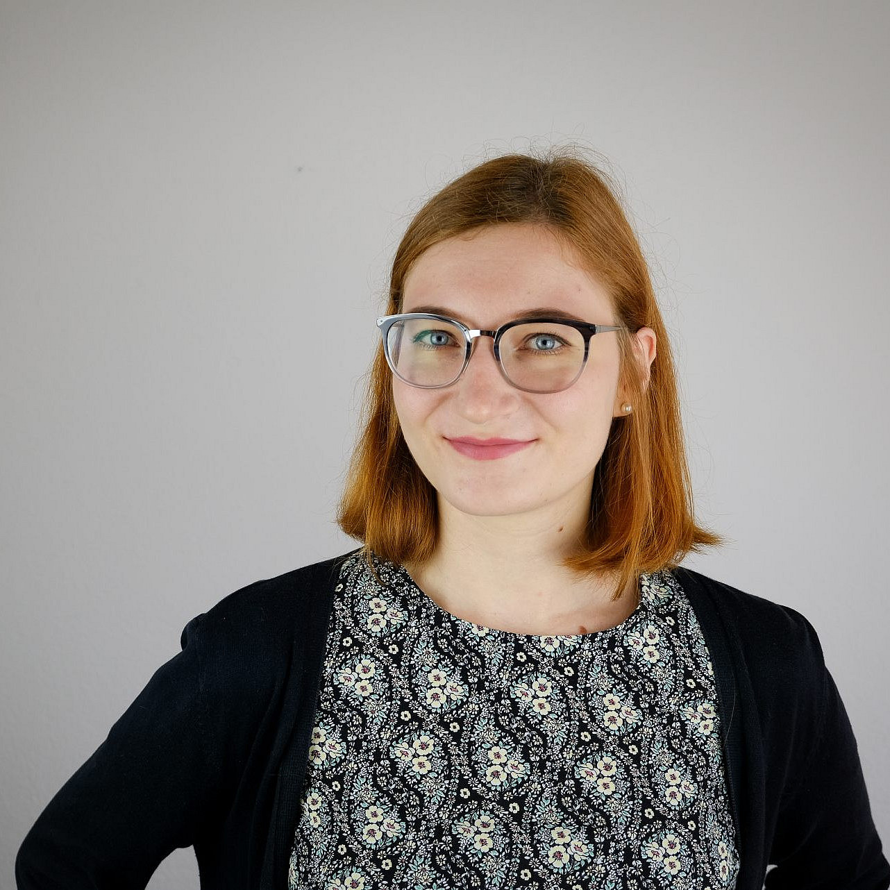 Porträtfoto einer lächelnden jungen Frau mit schulterlangen roten Haaren und einer Brille