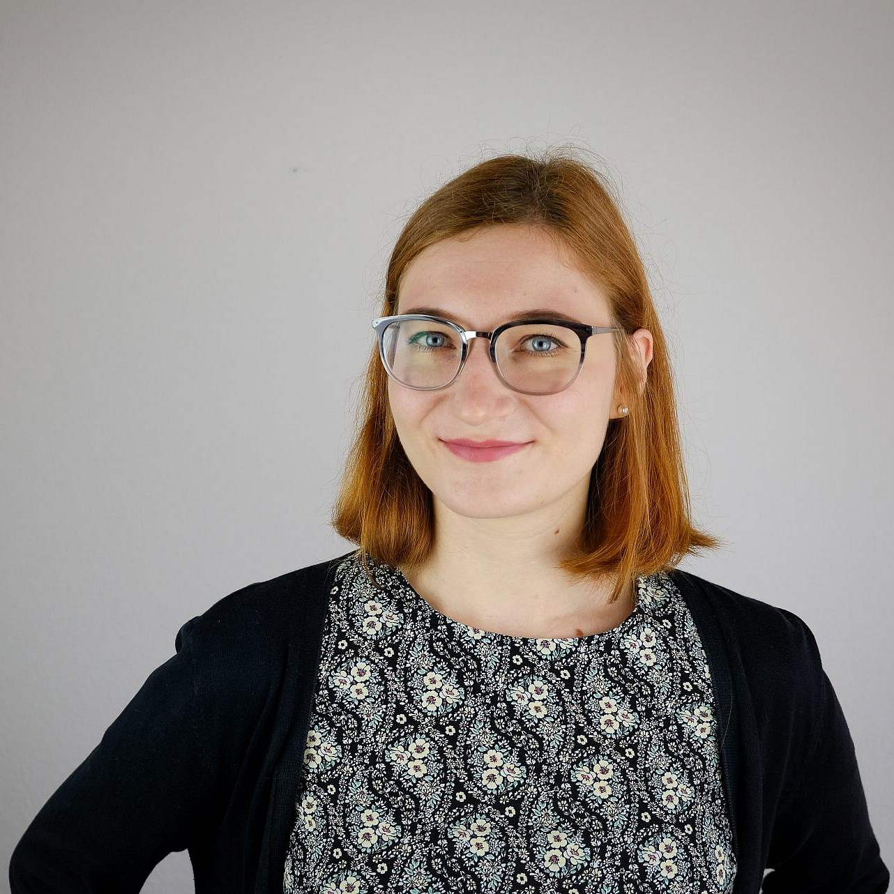 Porträtfoto einer lächelnden jungen Frau mit schulterlangen roten Haaren und einer Brille