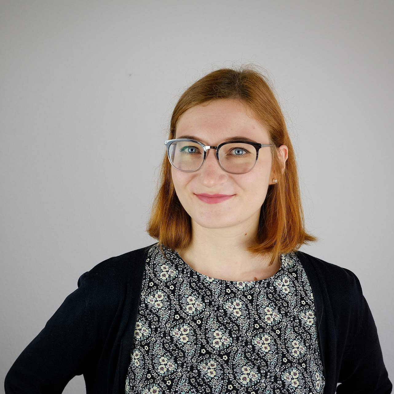 Porträtfoto einer lächelnden jungen Frau mit schulterlangen roten Haaren und einer Brille