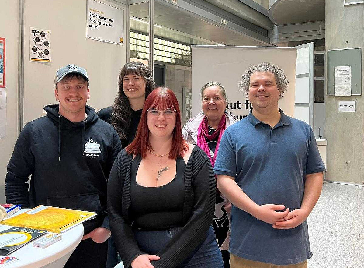 eine Professorin und 4 Studierende stehen vor einem Infostand mit Luftballons 