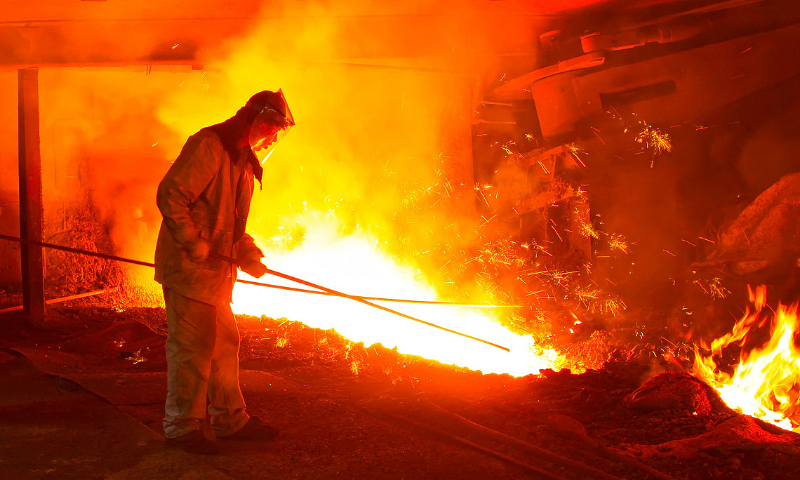 Worker in protective clothing in front of red-hot blast furnace