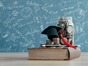 Book, on which a doctor's hat and a money box lie, in front of a written panel ©narawit - stock.adobe.com
