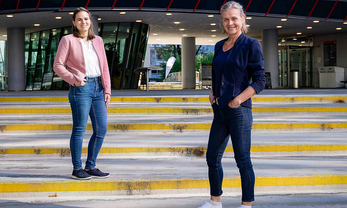 Two women are standing on the steps in front of a building