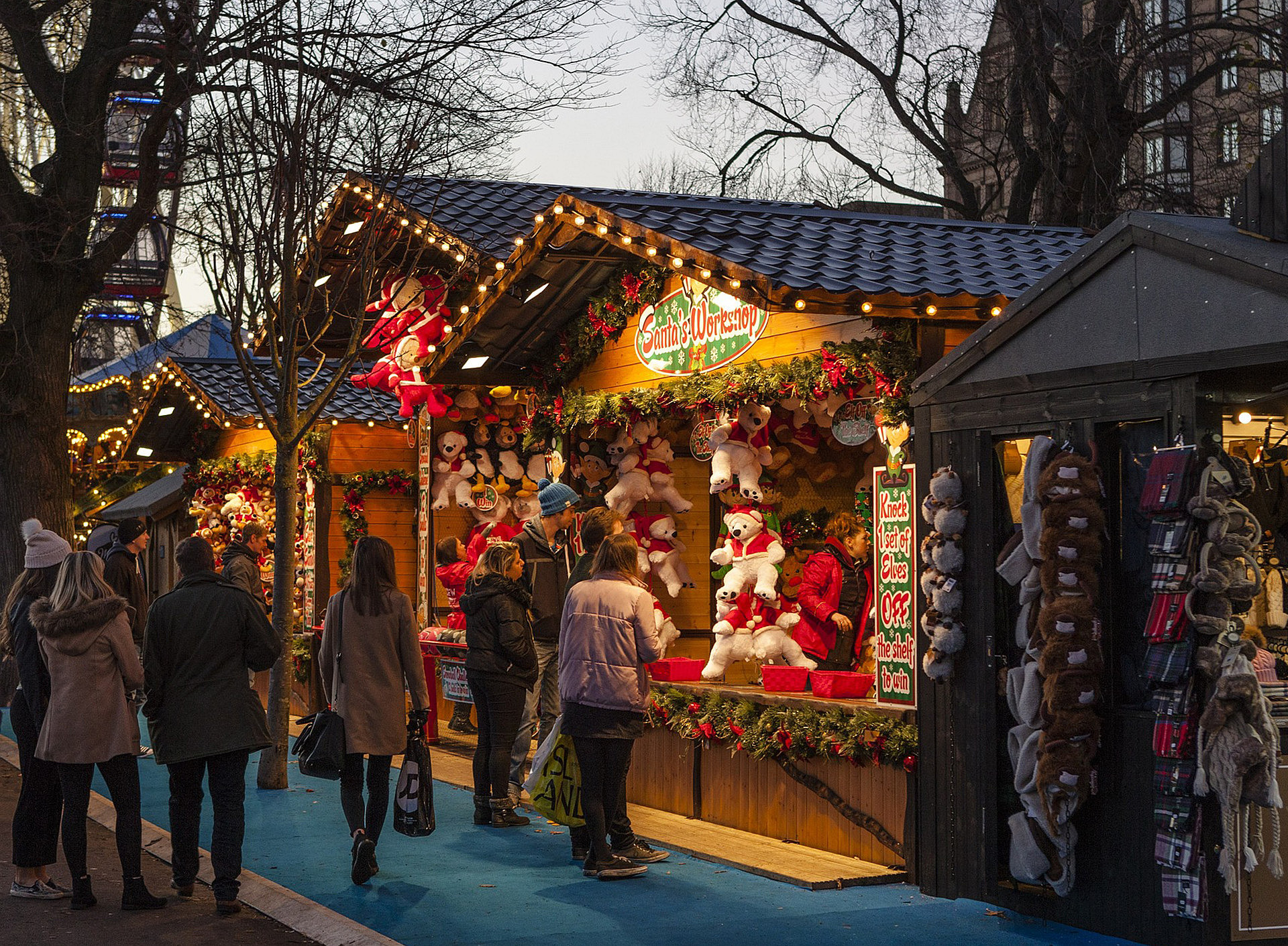 Weihnachtsmarkthütte, geschmückt mit viel weihnachtlicher Deko und einigen Personen die vorbeigehen und den Stand anschauen ©Pixabay