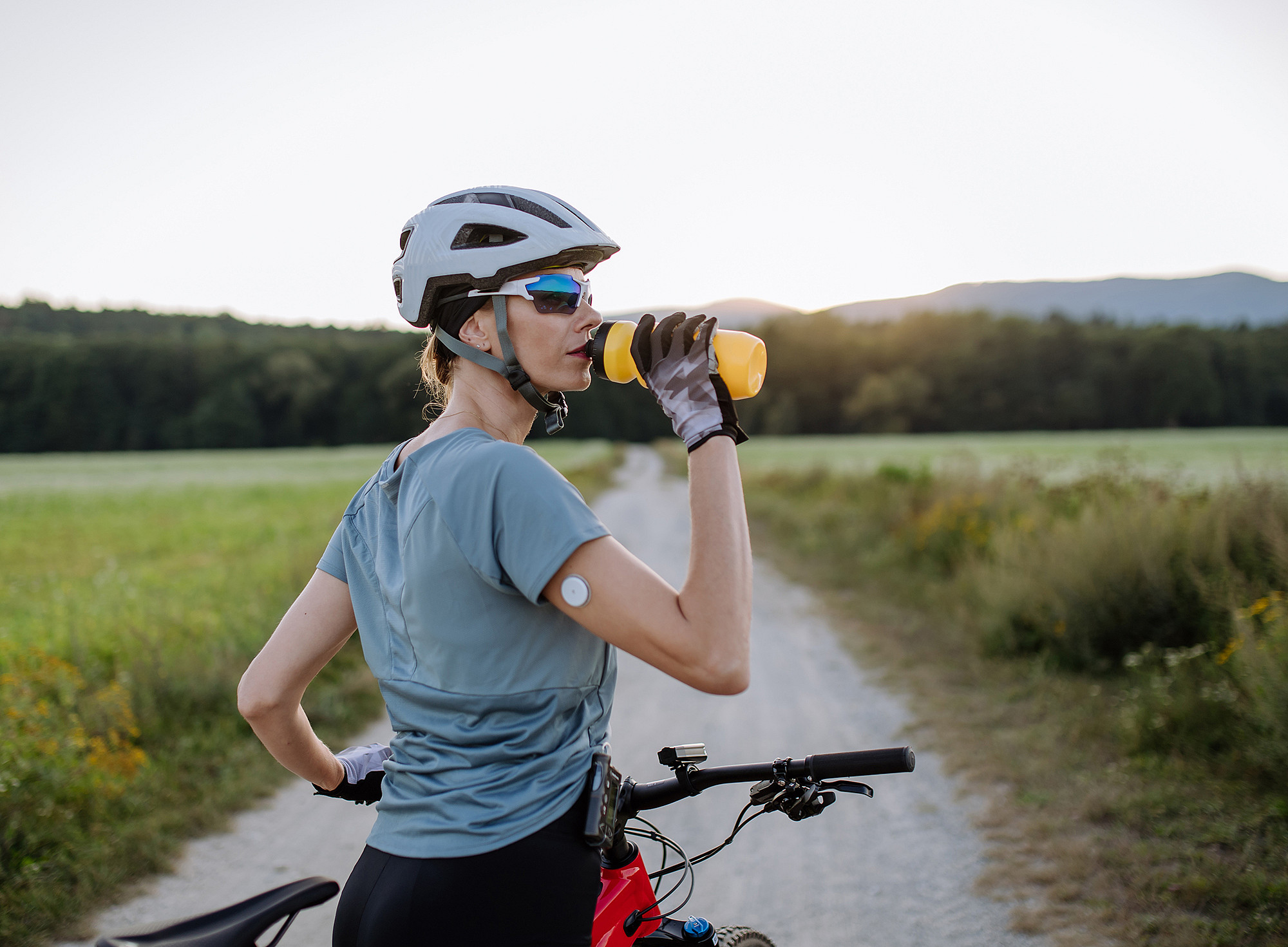 Radfahrerin mit Diabetes und Glukose-Monitor am Arm, die während einer Tour Wasser trinkt 