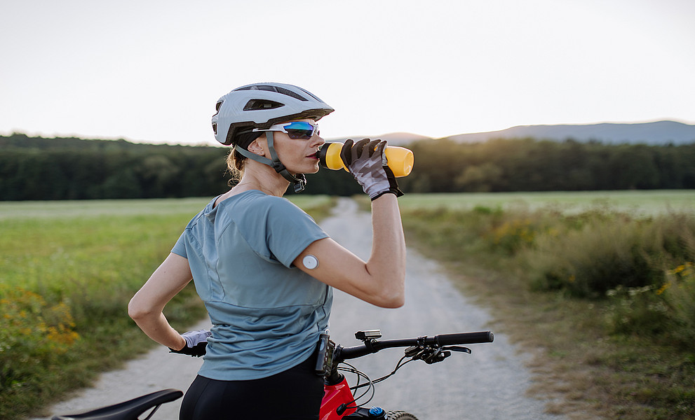Radfahrerin mit Diabetes und Glukose-Monitor am Arm, die während einer Tour Wasser trinkt