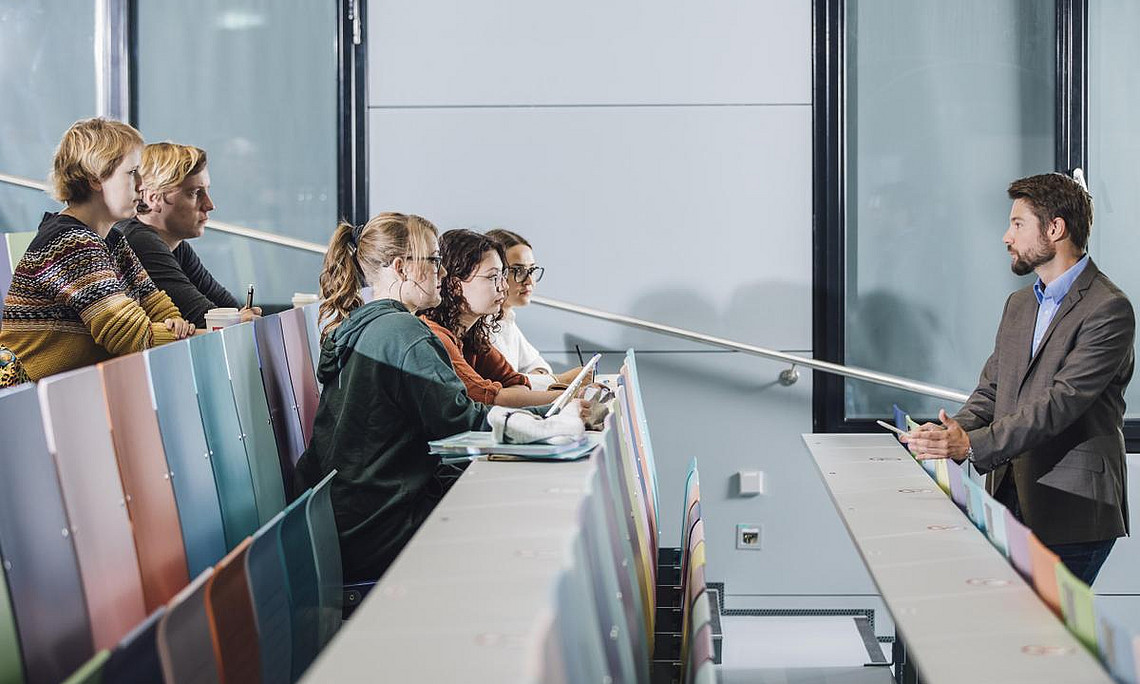 Ein Lehrender der Uni Graz steht vor den Studierenden im Lehrraum und hält einen Vortrag.