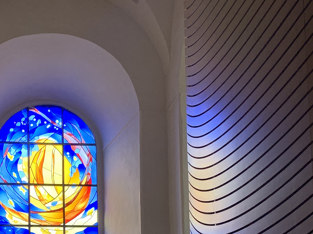 Blick auf ein modernes Glasfenster neben dem Oratorium des Franziskanerklosters Graz. Dargestellt ist ein in Orangetönen gehaltenes Segelboot umgeben von Blautönen ©Birgit Roth, Dekanat Theol Fakultät Graz