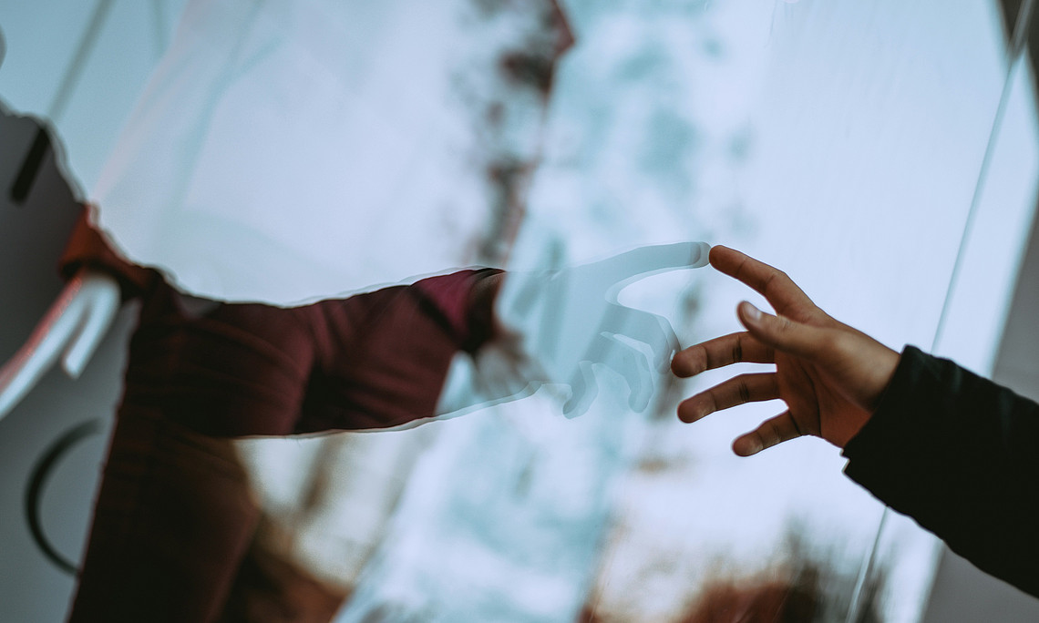 Eine Hand die sich im Fenster spiegelt. Hand berührt das Spiegelbild 