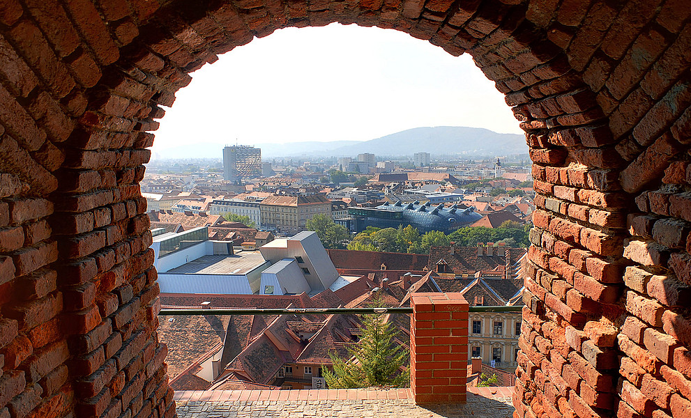 Blick durch einen Durchgang aus roten Ziegeln vom Grazer Schlossberg auf die Stadt