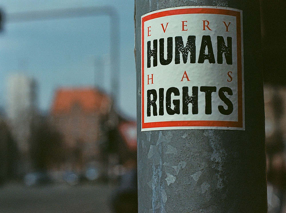 Poster mit der Aufschrift "every human has rights" auf grauer Säule vor verschwommenem Hintergrund ©Markus Spiske - unsplash