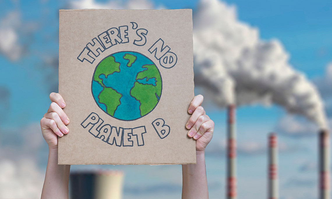 zwei Arme halten Schild hoch "There's no planet B", im Hintergrund rauchende Schlote