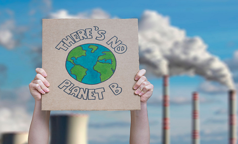zwei Arme halten Schild hoch "There's no planet B", im Hintergrund rauchende Schlote