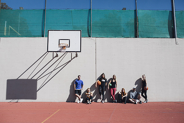 Am Basketballplatz sitzen und stehen sportlich angezogene Studierende angelehnt an eine Mauer, schräg über ihnen ist der Basketballkorb