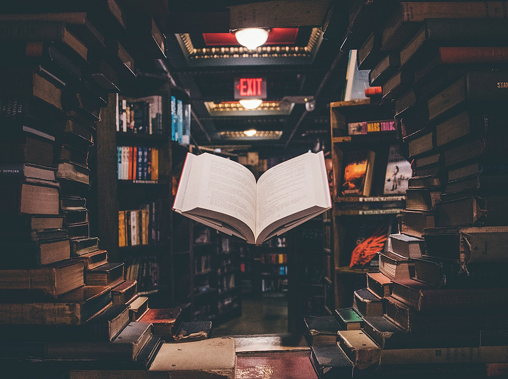 Ein aufgeschlagenes Buch schwebt zwischen Büchern in einer Bibliothek. ©Jaredd Craig/unsplash.com