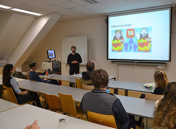in einem Seminarraum steht ein Mann vor einer Leinwand und hält einen Vortrag; in den Tischreihen sitzen ein paar Menschen und hören zu ©Uni Graz/Braunegger
