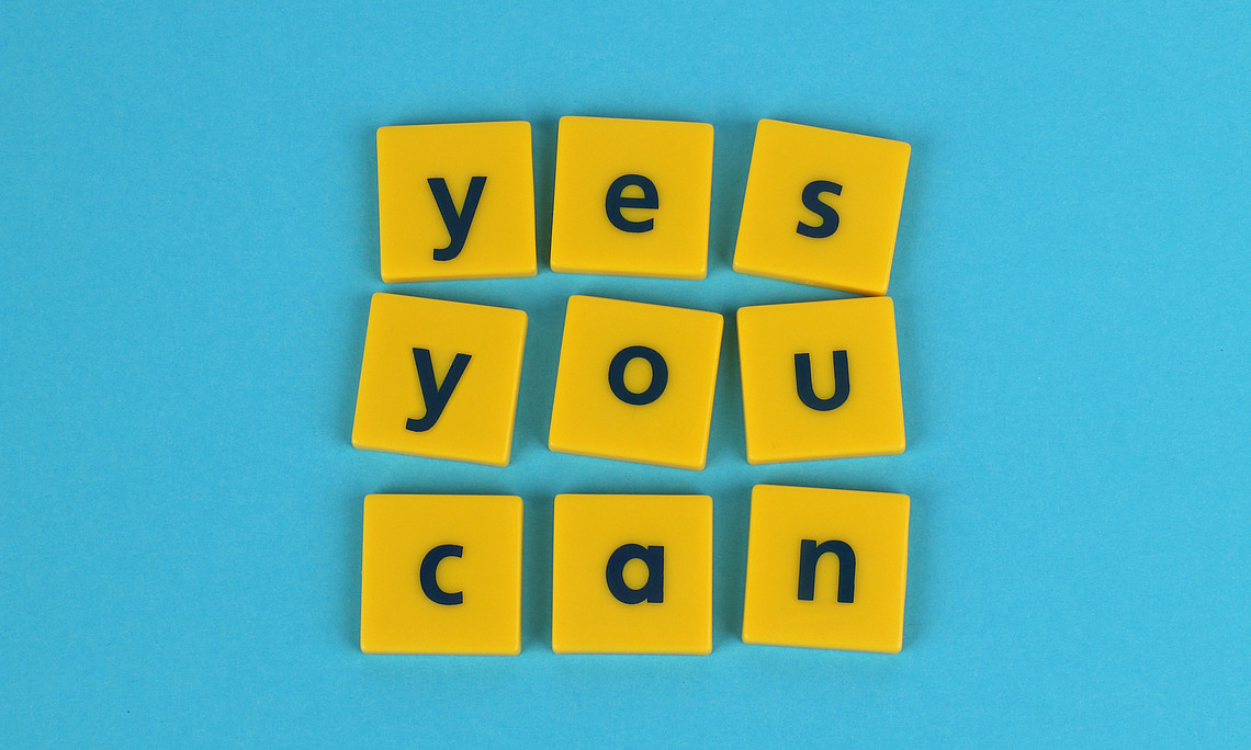 Gelbe Dominosteine auf blauem Hintergrund mit dem Schriftzug "Yes you can"