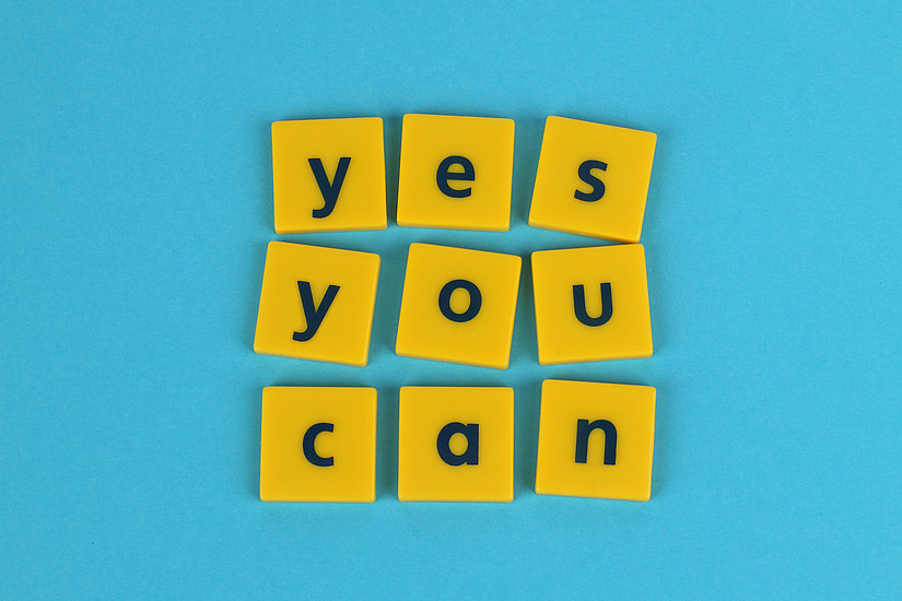Gelbe Dominosteine auf blauem Hintergrund mit dem Schriftzug "Yes you can"